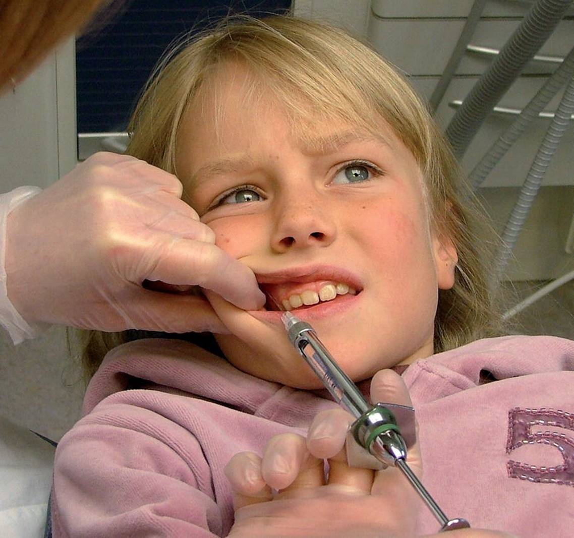 Photo of dentist making anesthetic injection to child’s gum before extracting tooth.