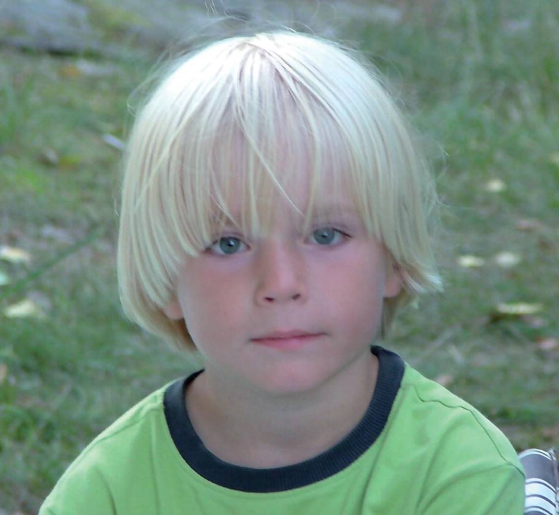 Photo displaying a blonde boy, with an apple cut, looking at the camera.